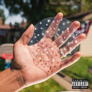There is a brown hand holding a clear CD with holes around it. There is a house in the background with green grass.
